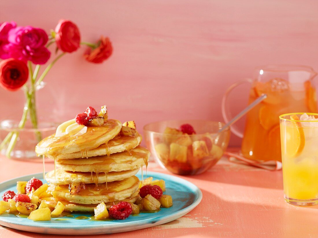 Gestapelte Pancakes mit Obst, Fruchtsaft und Blumen