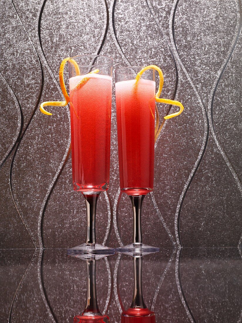 Zwei rote Cocktails mit Zitronenspiralen auf spiegelnder Oberfläche