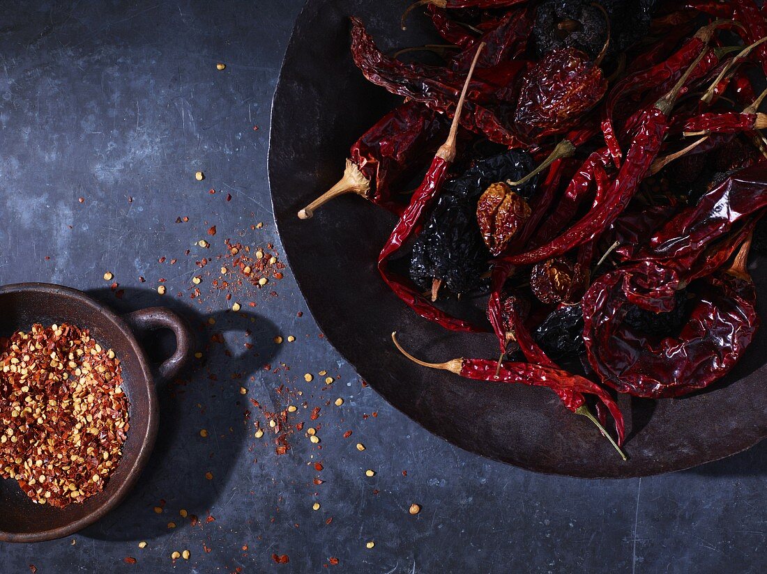 Dried chilli Peppers and chilli flakes in bowls (seen from above)