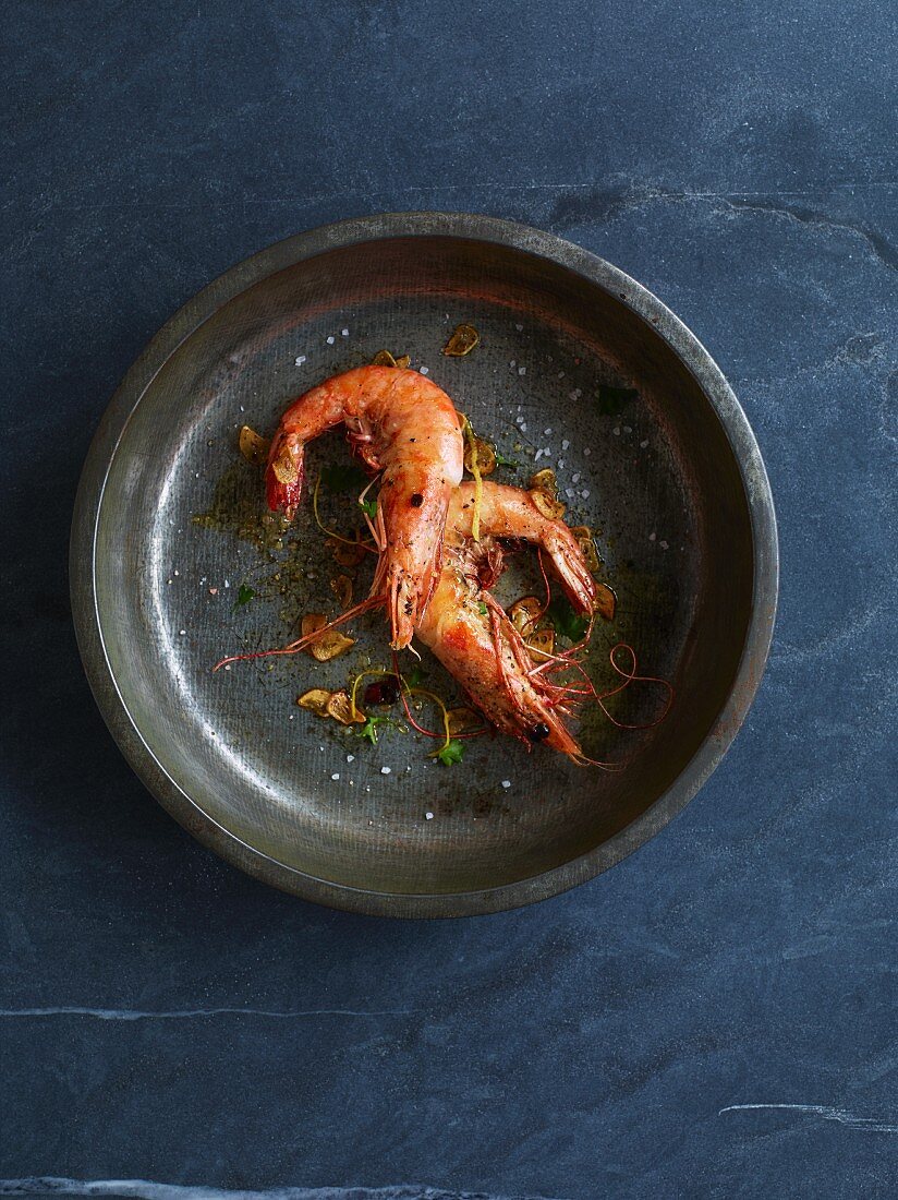 Two sauteed prawns in metal dish (seen from above)