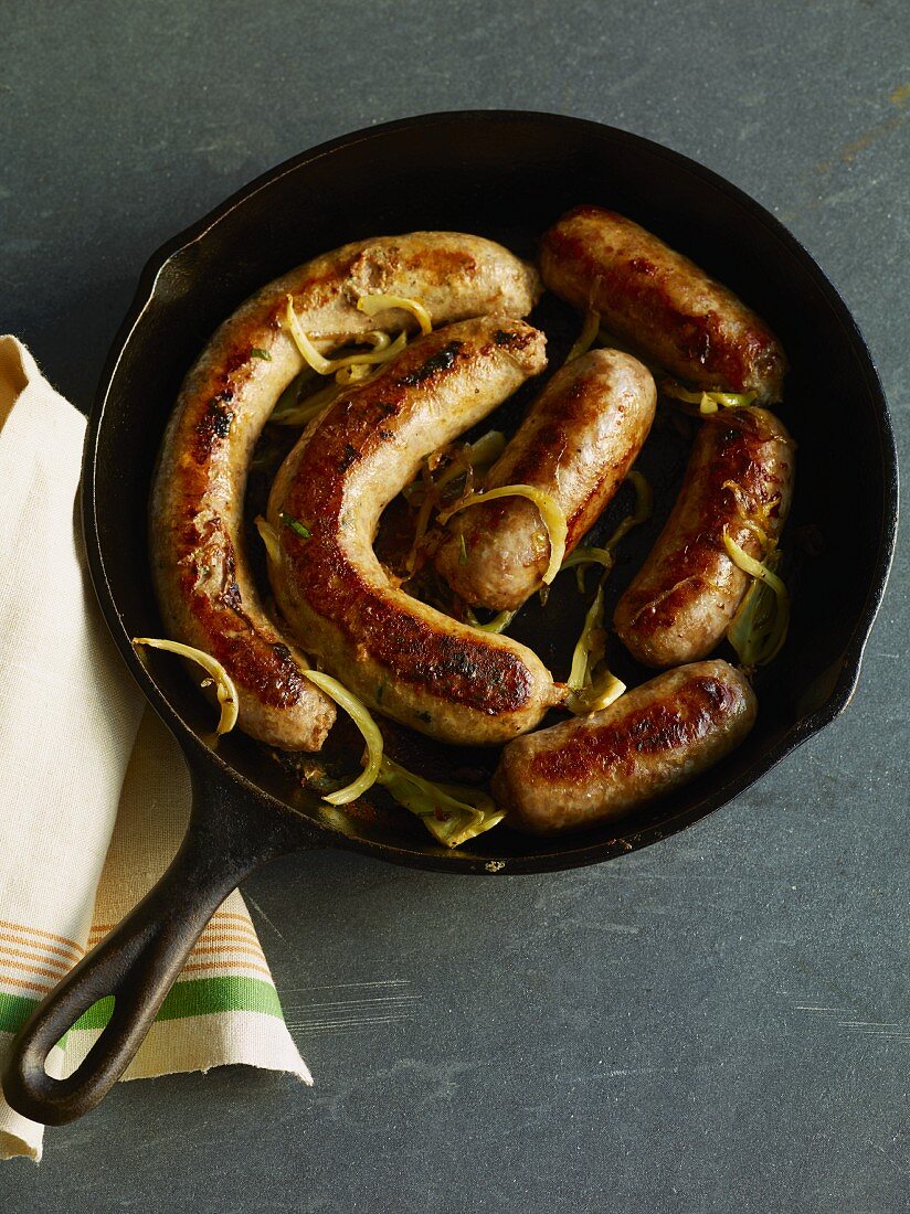 Fried sausages with onions in cast iron pan