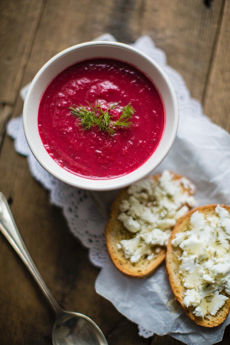 Beetroot soup served with slices of bread spread with cheese