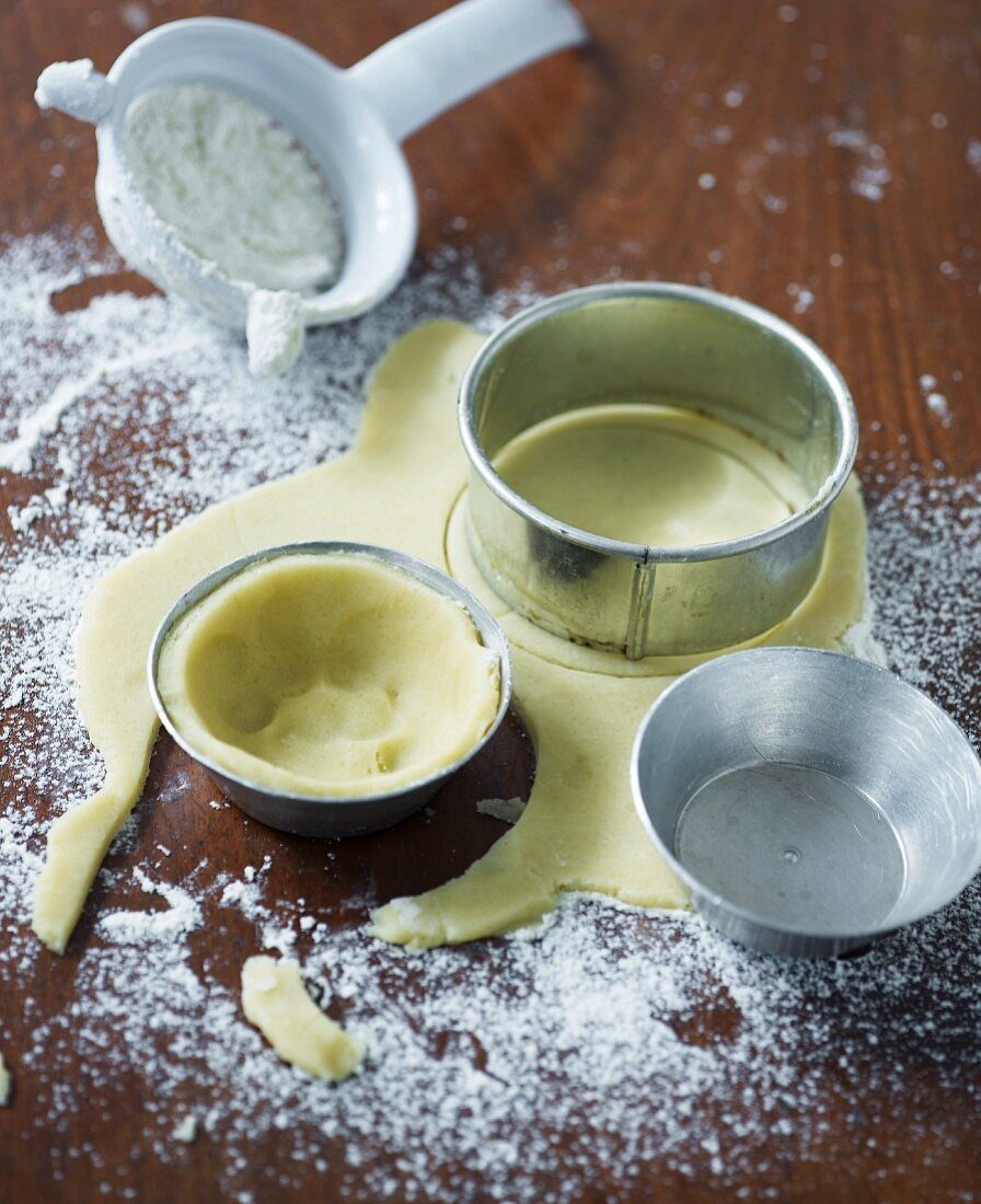 Raw shortcrust pastry in baking tins and cutters on a floured work surface