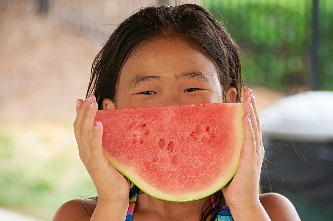 A little girl eating a seedless watermelon at a pool party