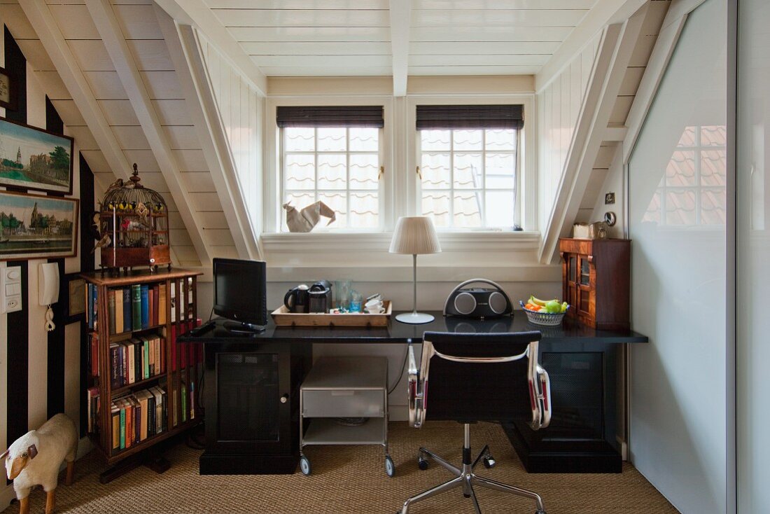 Desk, classic Eames swivel chair and other small items of furniture next to bookcase in attic room