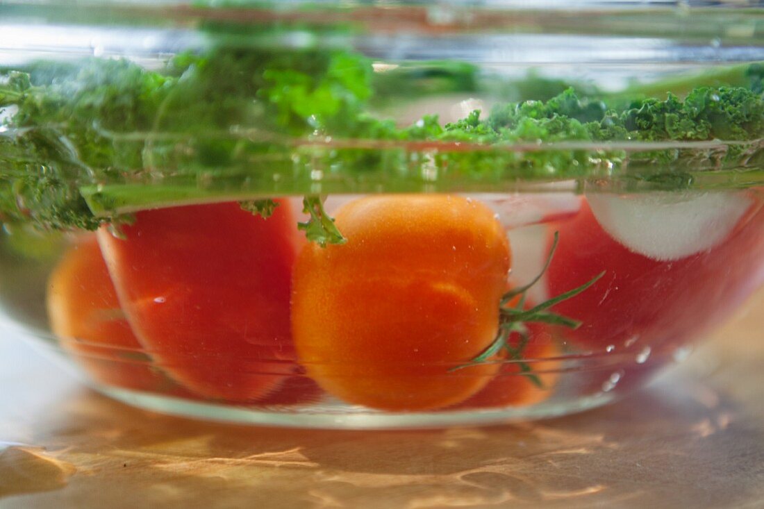 Tomatoes and green kale in a bowl of water (close-up)