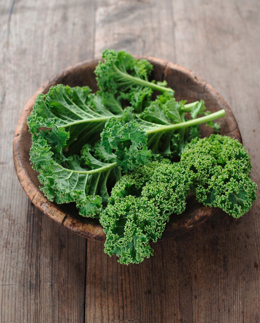 Green kale in a wooden bowl on a wooden surface