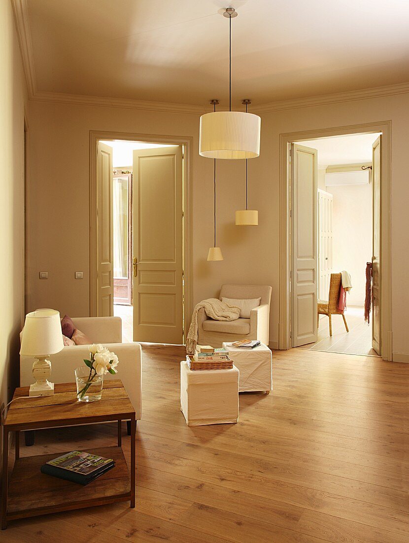 Lounge area in foyer with open double doors and traditional ambiance; pouffes and armchairs with white loose covers under pendant lamps with white lampshades