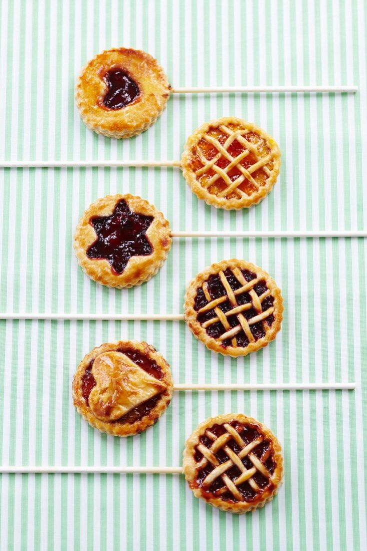 Six jam tarts on sticks decorated with stars, hearts and lattice toppings