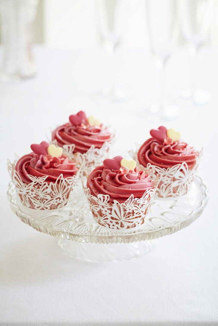 Cupcakes mit rosa Zuckerguss und Zuckerherzen in weissen Schmetterlingsschalen
