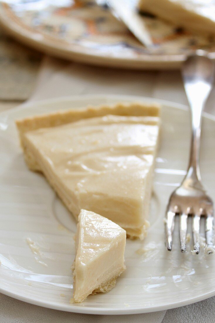 A slice of lemon cream tart on a plate with a fork
