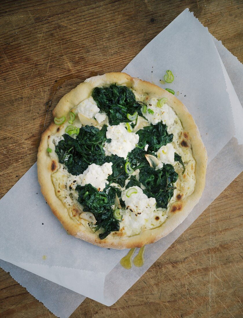 Spinach pizza on a piece of paper on a wooden table