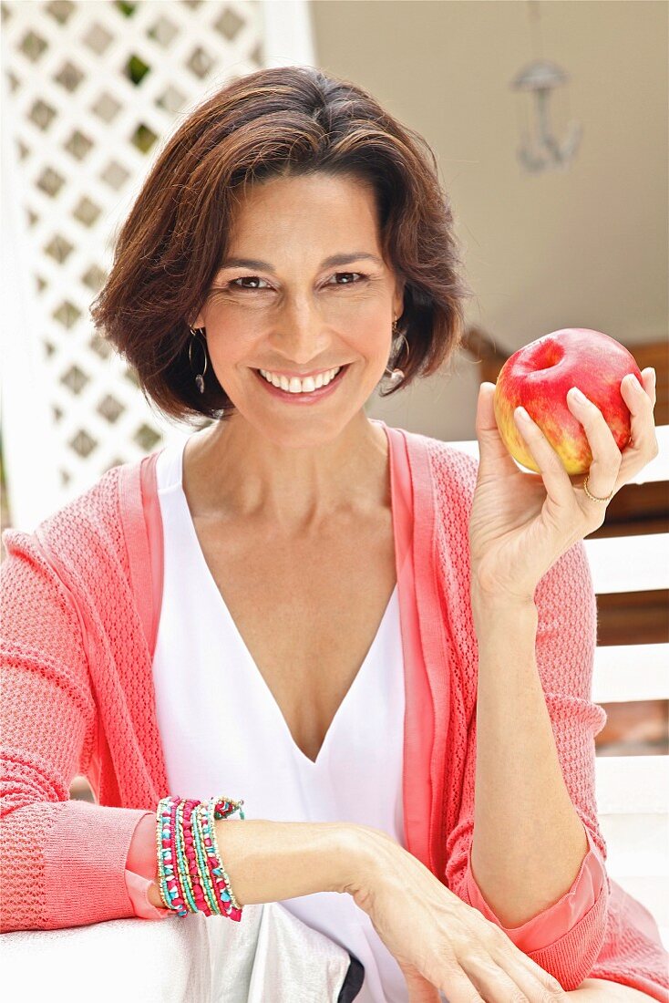 Dark-haired woman wearing top and cardigan holding apple