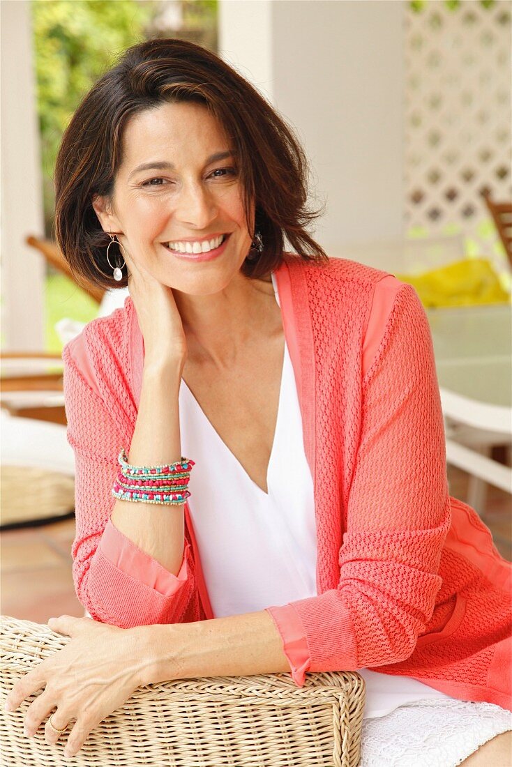 A dark-haired woman sitting in a wicker chair wearing a top and a cardigan