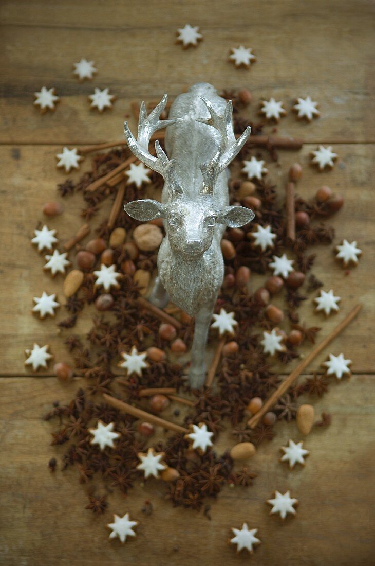 A stag figurine surrounded by nuts, cinnamon stars, cinnamon sticks and star anise