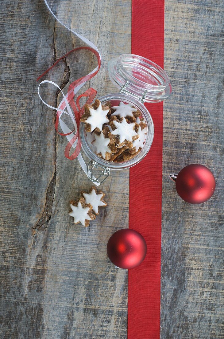 Cinnamon stars in a jar with a flip-top lid next to Christmas tree baubles and a ribbon