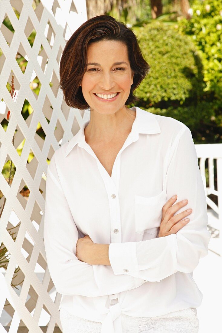 A brunette woman with her arms folded wearing a white blouse