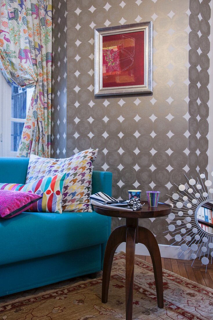 Antique side table in front of light blue couch against patterned wallpaper