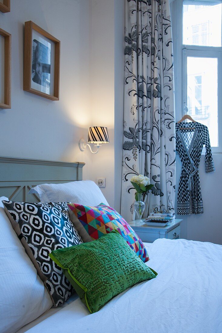 Colourful scatter cushions on bed in front of black and white patterned curtains