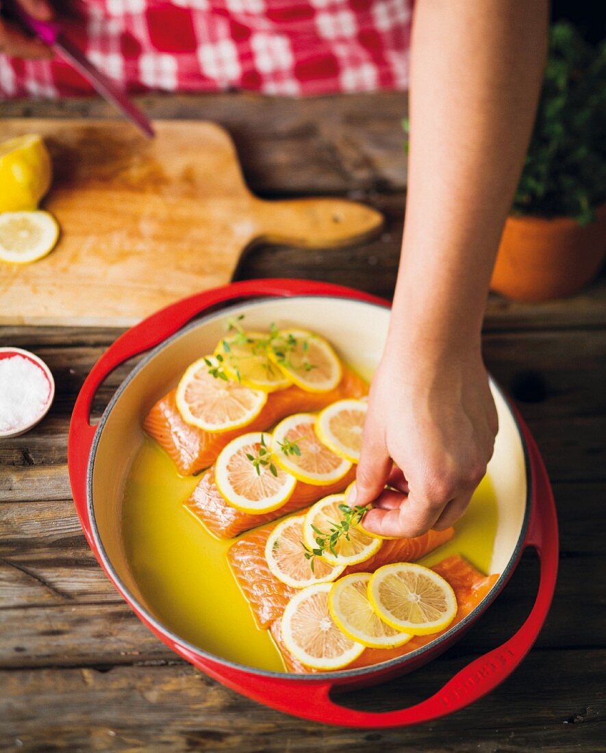Salmon steaks being topped with lemon slices and thyme