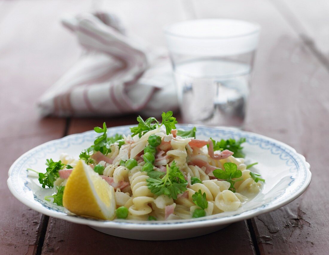 Pasta with a creamy sauce, ham, peas, parsley and lemons