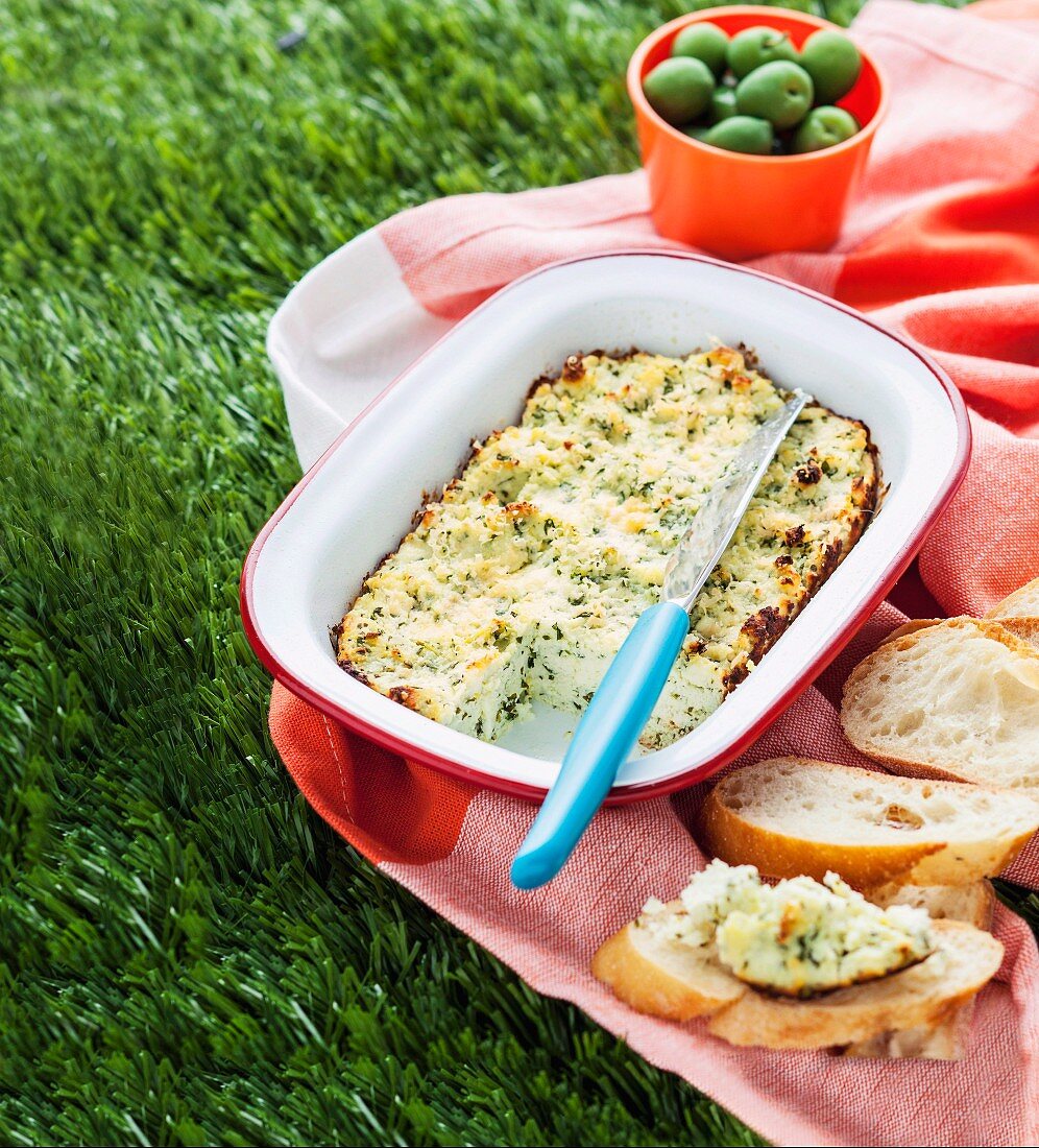 Gebackener Ricotta mit Kräutern, Baguette und Oliven auf einer Picknickdecke