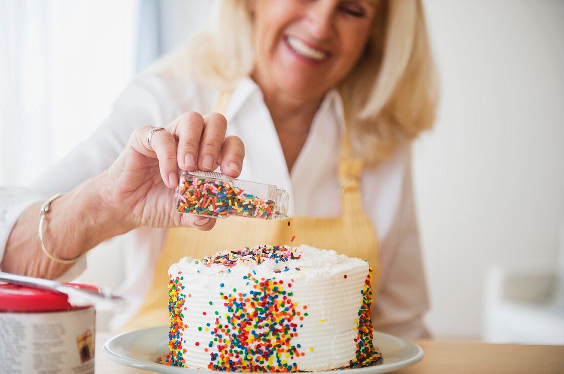 A woman decorating a cake with sugar sprinkles