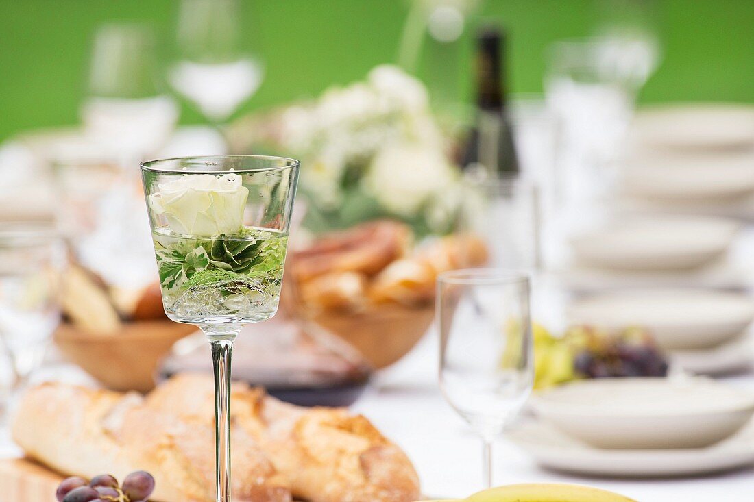 A rose in a glass on a table laid in a garden