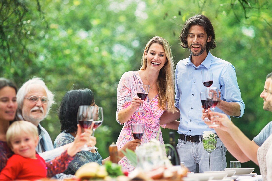 A couple raising glasses of red wine at a garden party