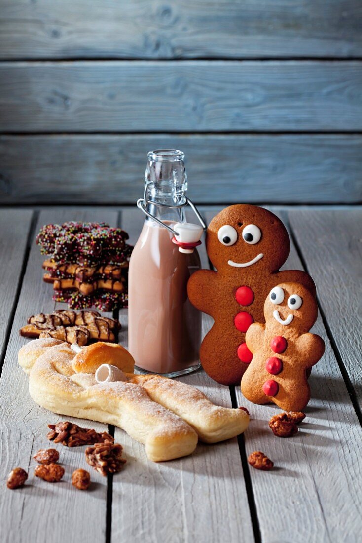 Zwei Lebkuchenmänner, Kakaoflasche, Stutenkerl und Weihnachtskekse auf grauem Holz