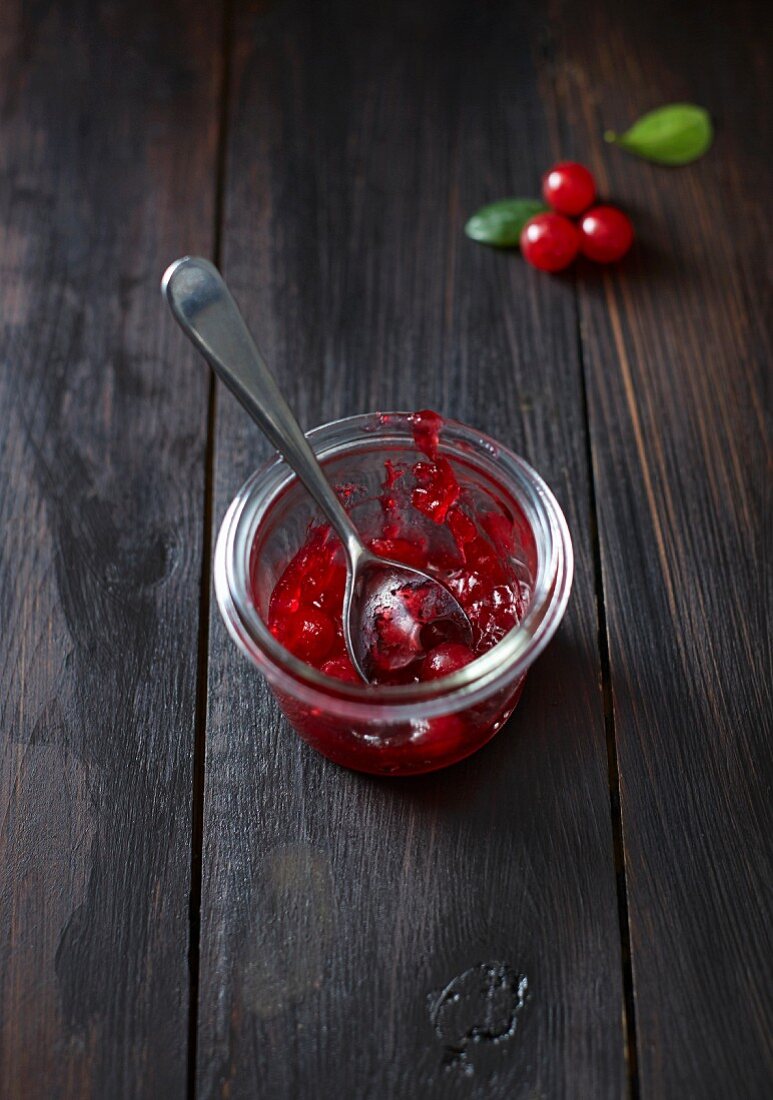 Cranberry sauce in a glass with a spoon on a dark wooden surface