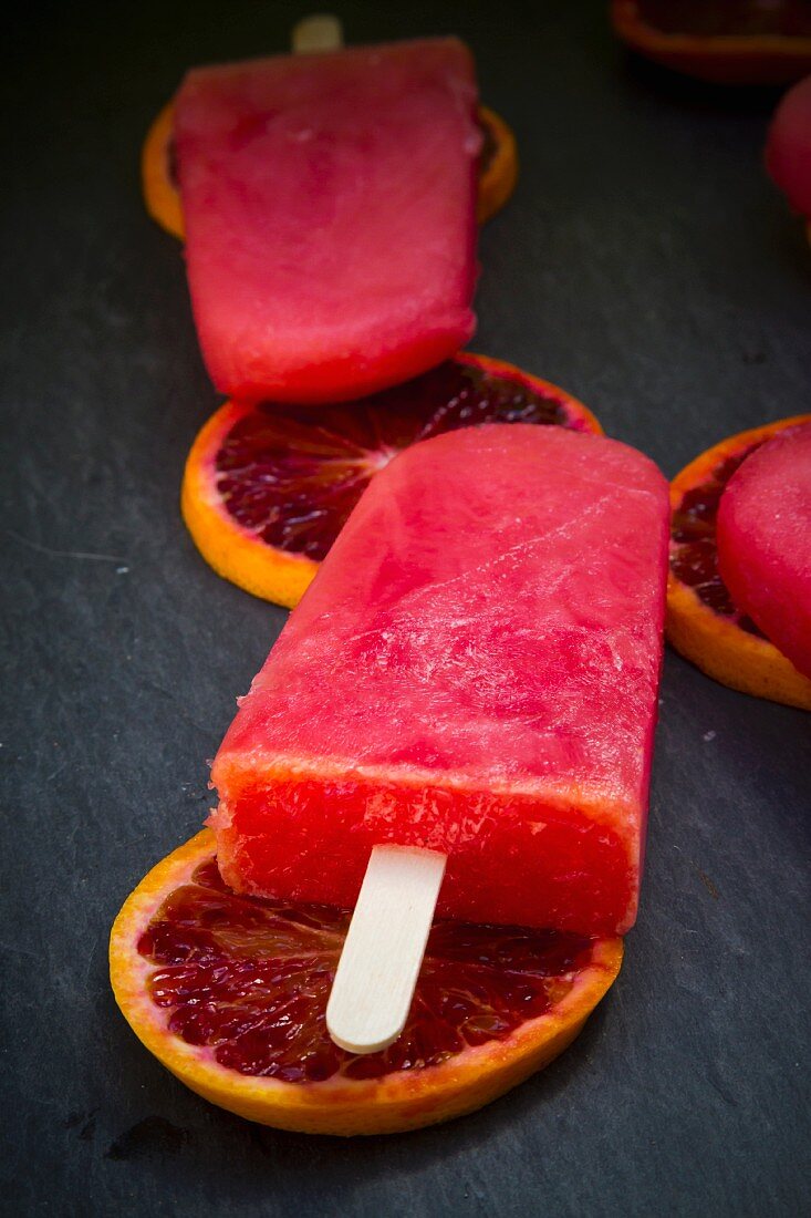 Blood orange ice lollies and blood orange slices on a slate surface