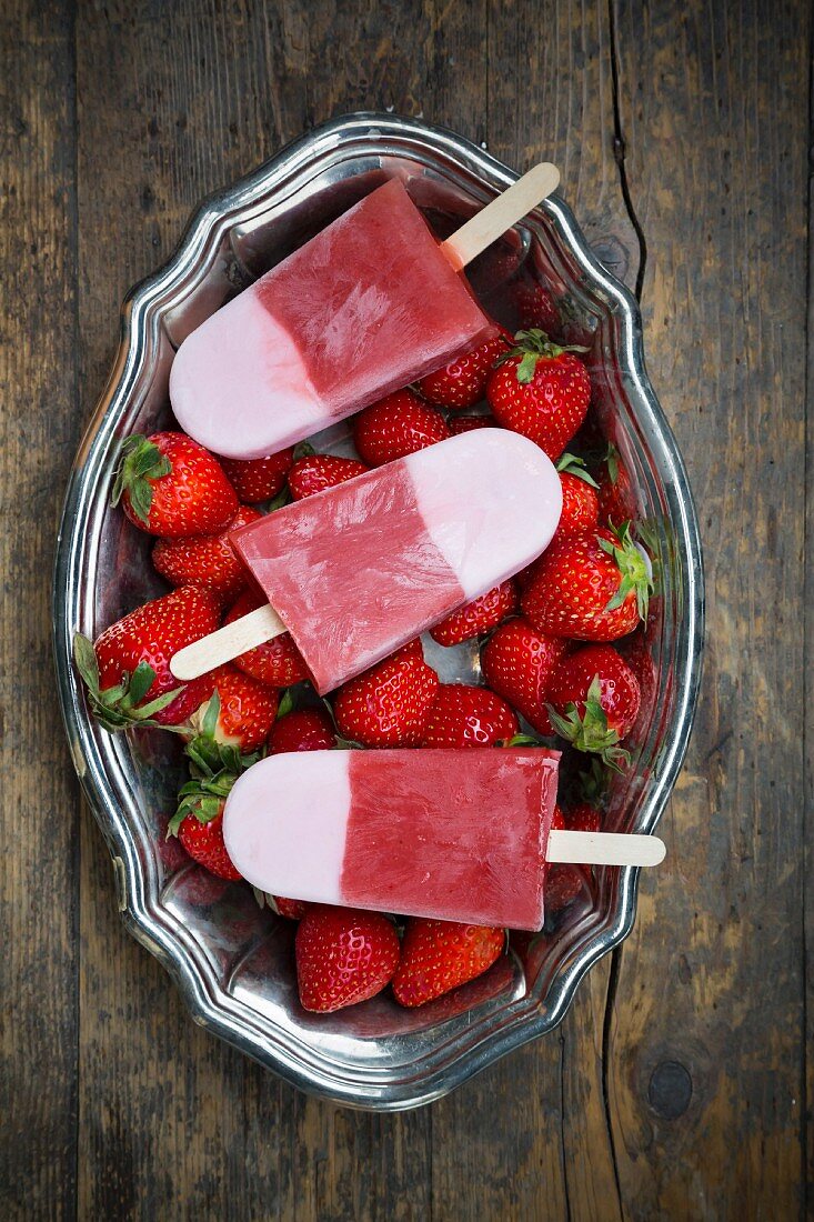 Strawberry ice lollies and strawberries in a metal bowl