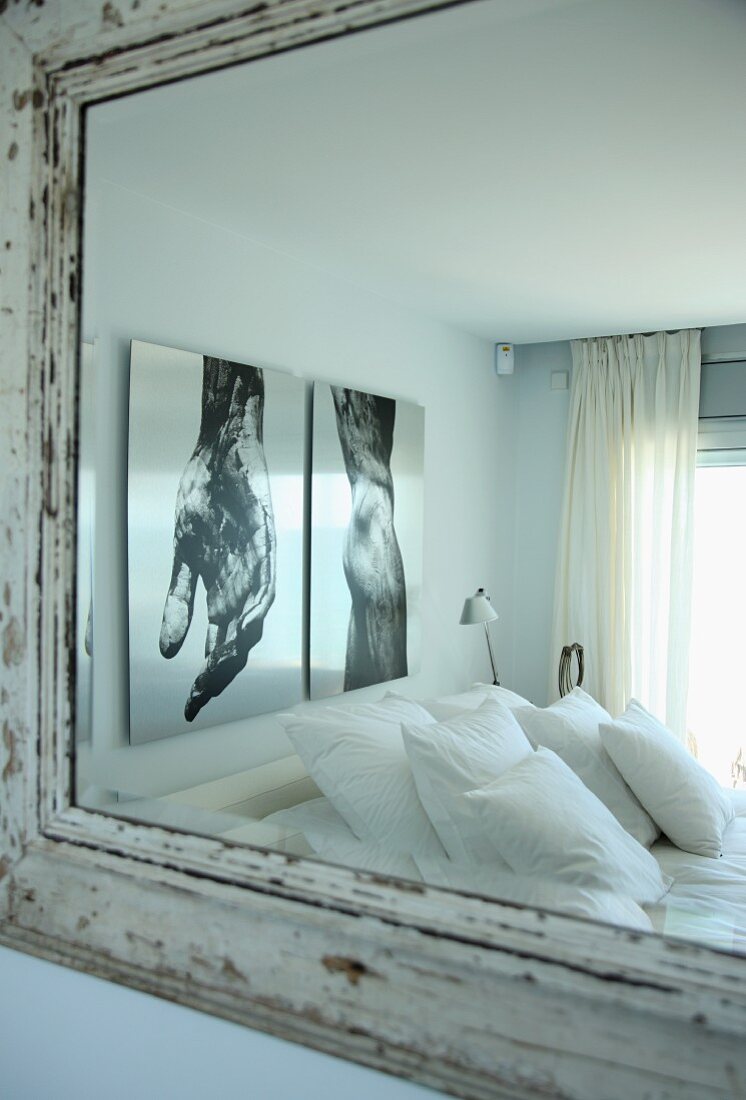 Stacks of pillows on bed below large photos on wall reflected in wall-mounted mirror