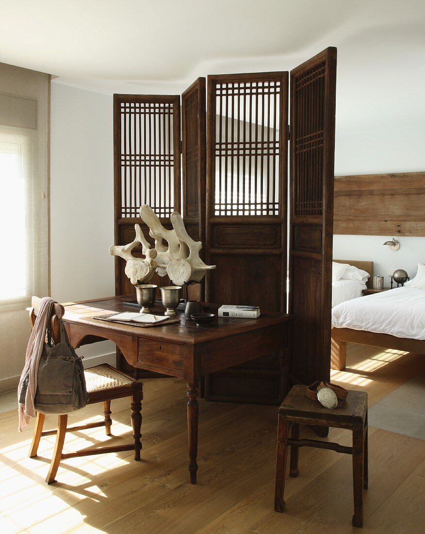 Antique writing desk and chair against wooden screen in front of sleeping area in simple room with well-kept wooden floor