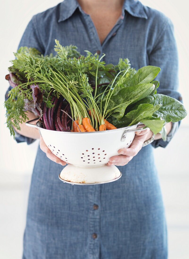 A woman holding a colander of fresh vegetables