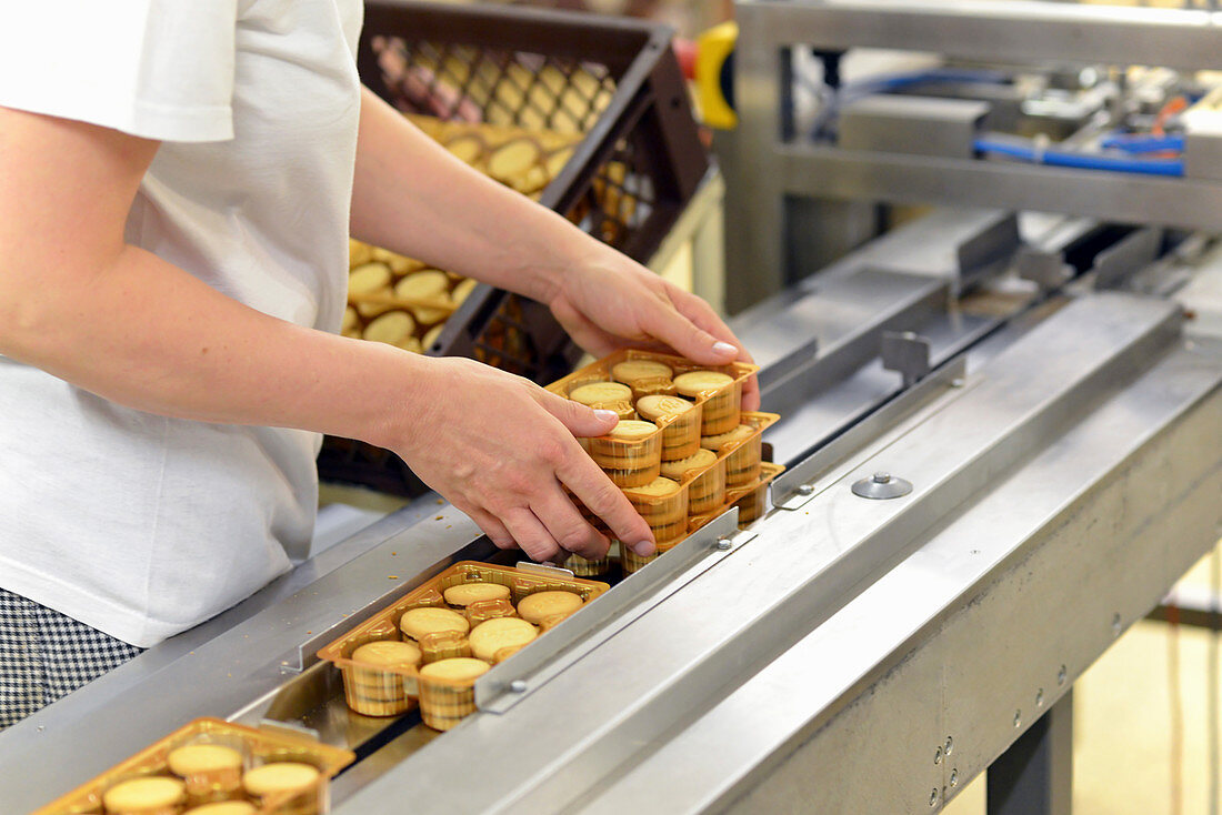 Frau nimmt verpackte Kekse vom Förderband in einer Backfabrik