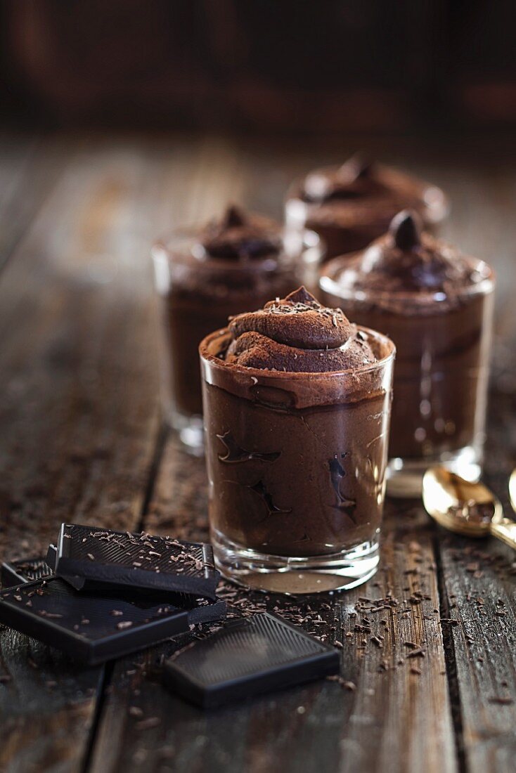 Glasses of vegan mousse au chocolat and dark chocolate on a wooden surface