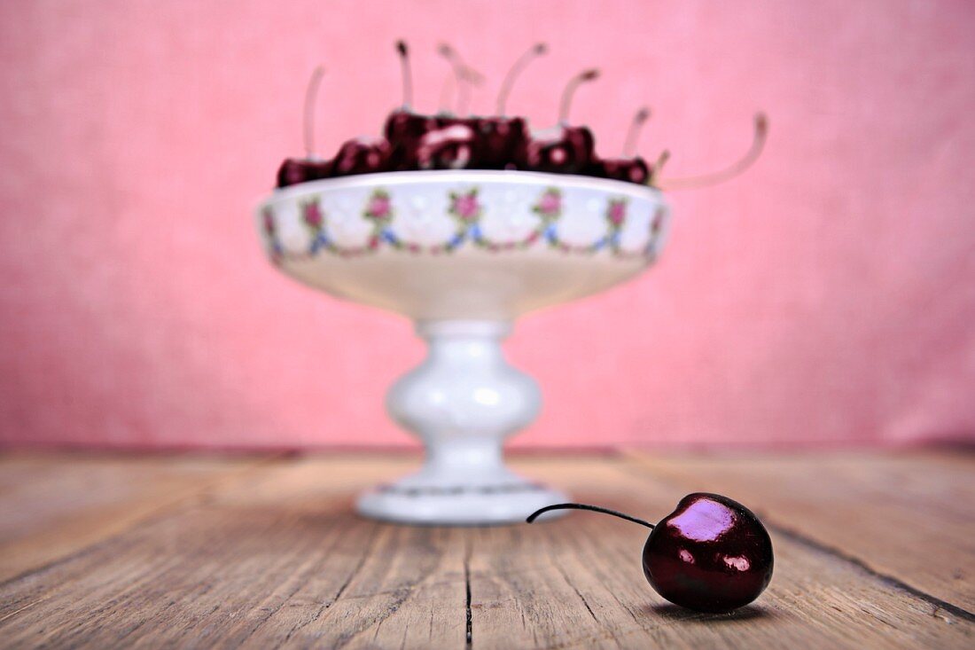 Cherries in a bowl on a wooden table with one cherry in the foreground