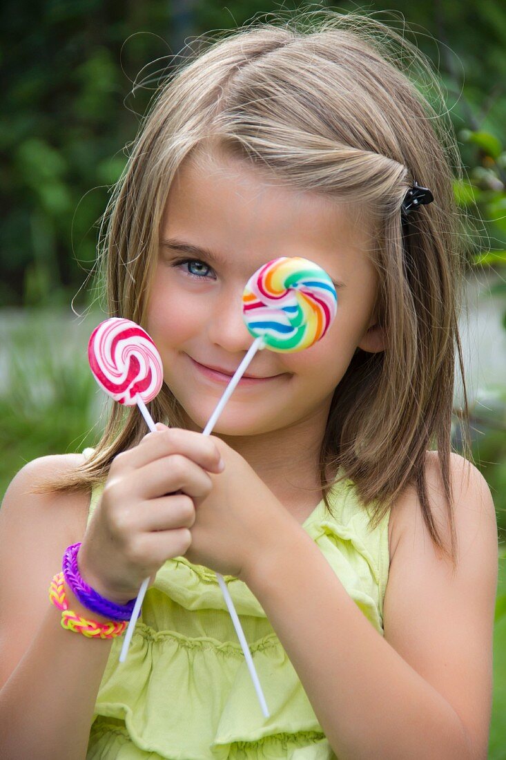 A little girl holding two lollipops