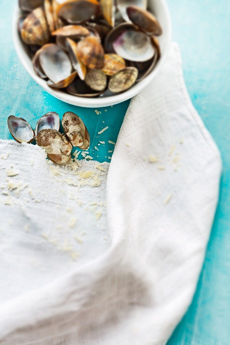 Empty clamshells in a bowl and on a table with grated Parmesan crumbs and a linen cloth