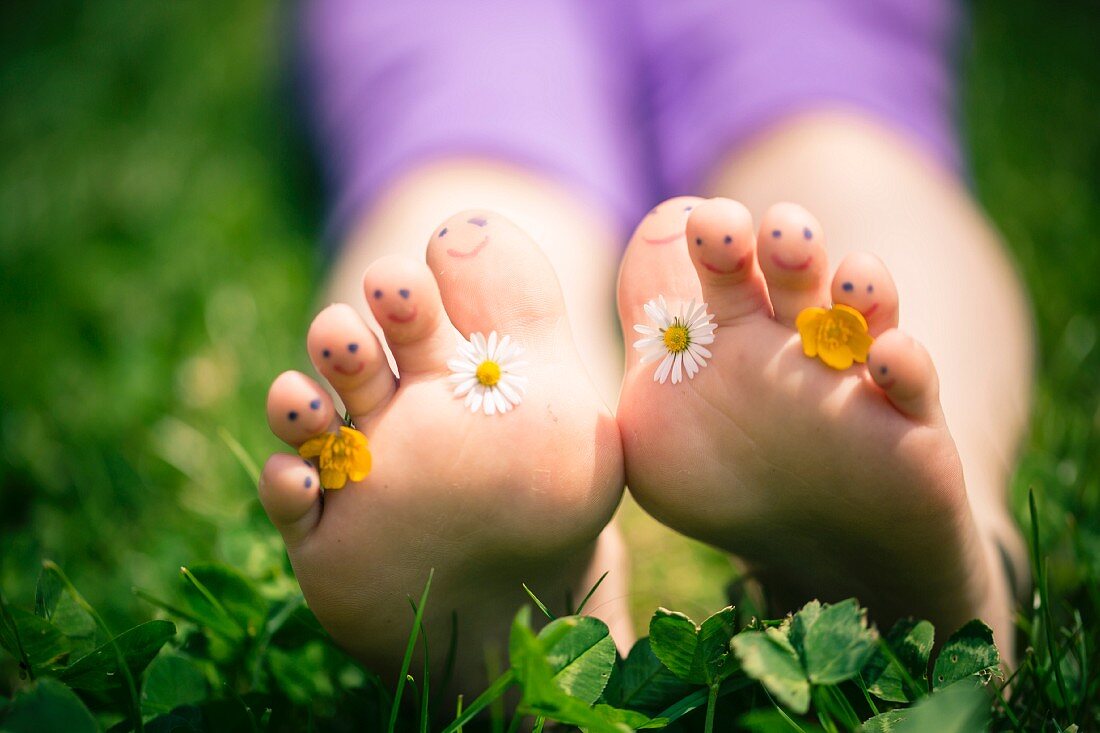 Little girl's toes decorated with daisies and buttercups and with drawn-on smiley faces