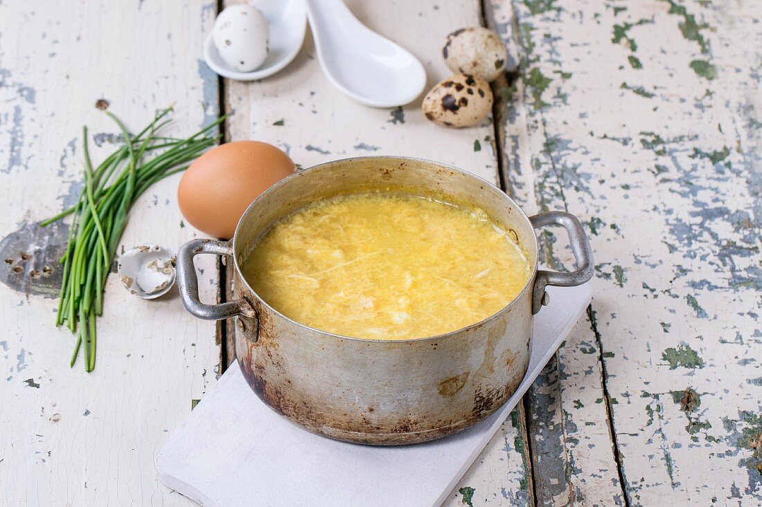 Egg drop soup in an old pot with ingredients next to it