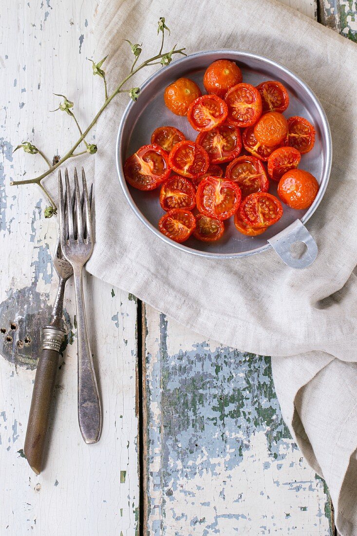 A bowl of baked cherry tomatoes in a bowl on an old wooden table (seen from above)