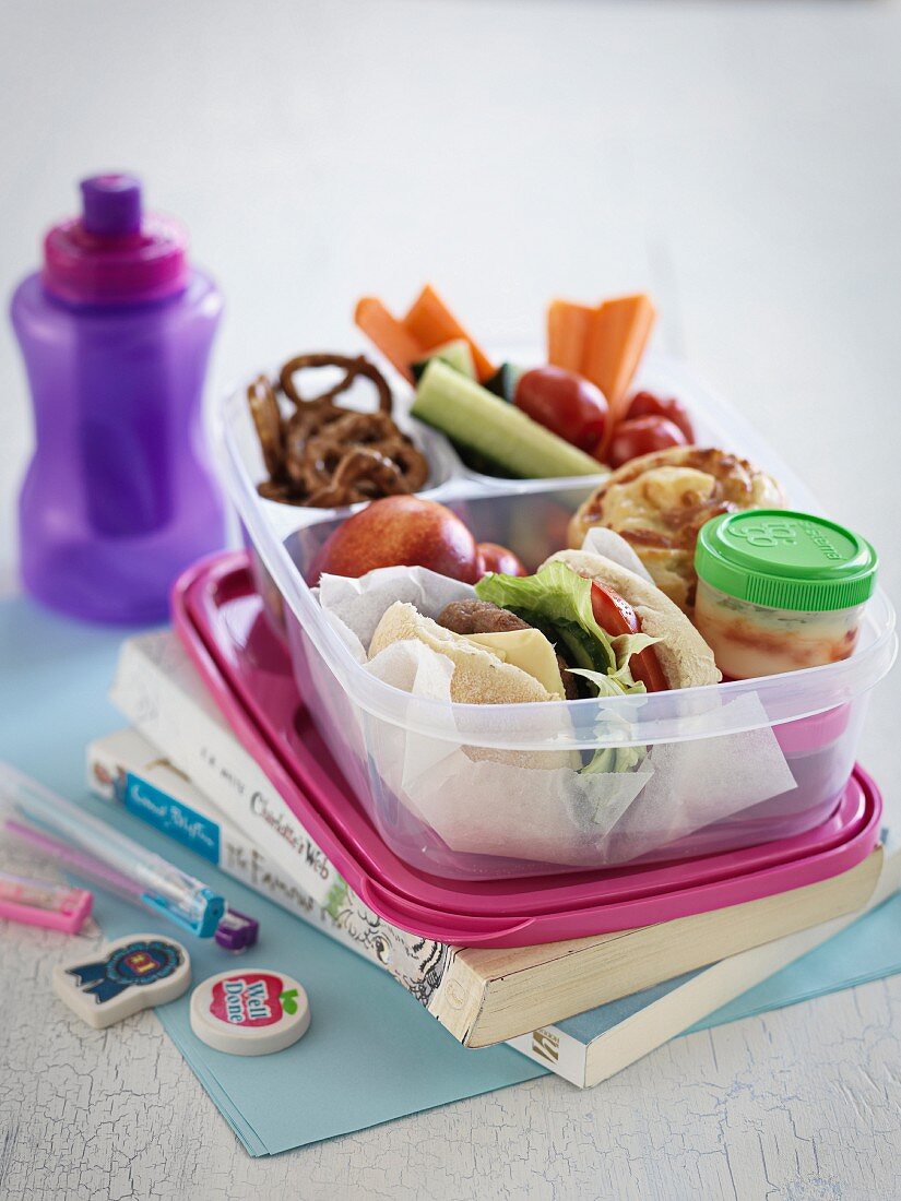A lunch box with a sandwich, fruit, vegetables and salted pretzels for school