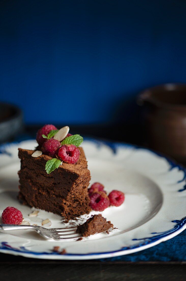A slice of dark chocolate cake with raspberries, mint and liquid cream