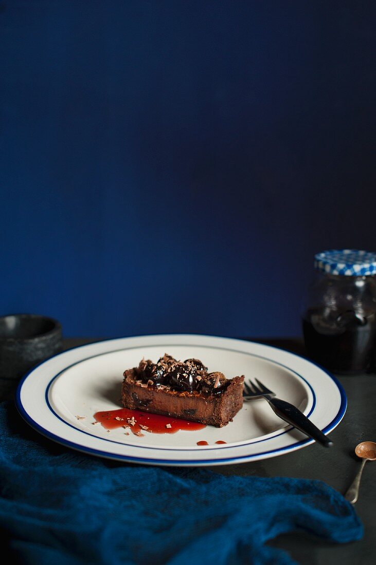 Ein Stück dunkler Schokoladen-Kirsch-Kuchen auf weißem Teller mit blauem Rand und Gabel
