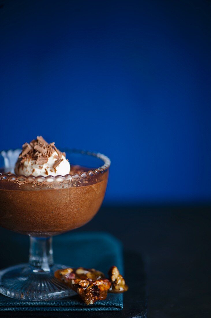 Dunkles Schokoladenmousse im Dessertglas mit Schlagsahne, Schokoladenspänen und Pecannusskrokant