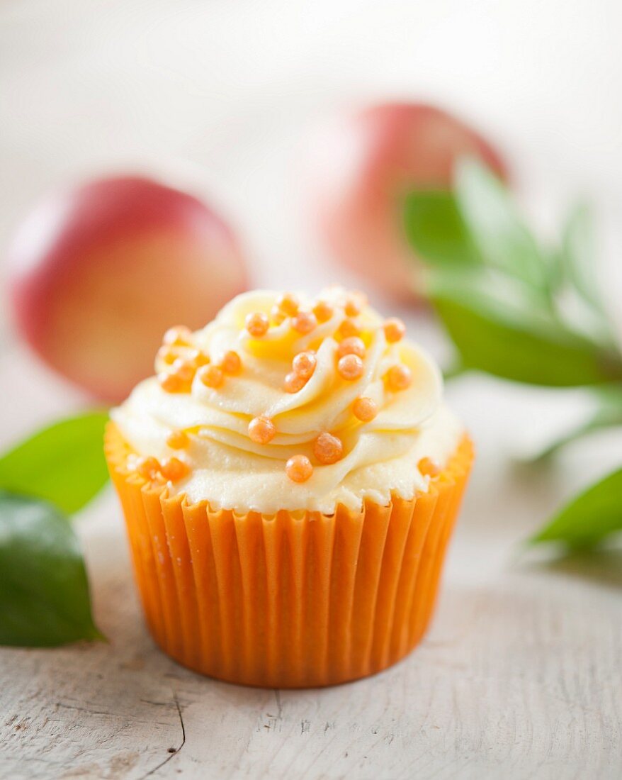 A cupcake with nectarine cream and orange sugar pearls
