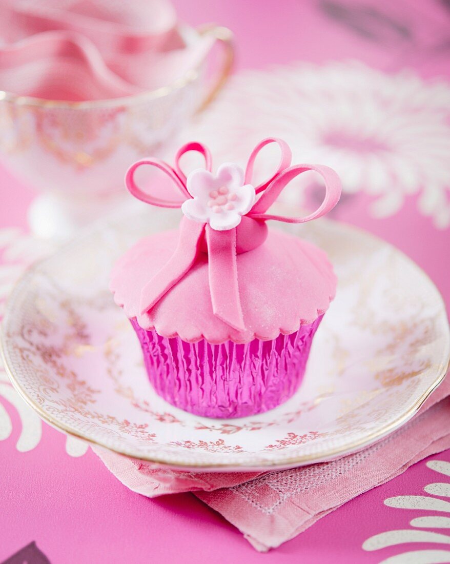 A pink flower cupcake on a gilded plate